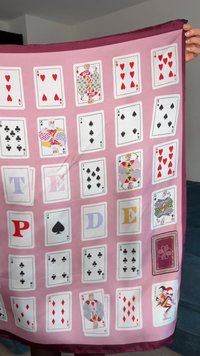 Seidenschal mit einem rosa Hintergrund, auf dem verschiedene Spielkarten, darunter Herzen und Pik, sowie dekorative Buchstaben in einem Rastermuster angeordnet sind.