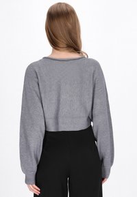 Pulover gri scurt cu o textură fină, mâneci largi și un decolteu subtil, asociat cu pantaloni negri cu talie înaltă.