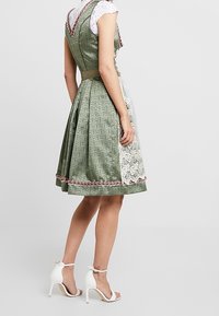 Robe verte à motifs avec un panneau en dentelle blanche, ornée d'un galon rouge à l'ourlet et à l'encolure. Associée à des sandales blanches à talons.