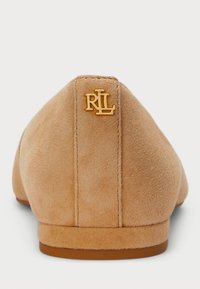 Bailarina de camurça beje com um salto baixo, apresentando um logo dourado RL na parte de trás. Textura suave e design minimalista.