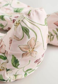 Õrnast kangast lilleline kaelapadi, kus on roosa taust roheliste viinapuude ja heledate roosade lilledega. Kaarjas, pehme kuju.