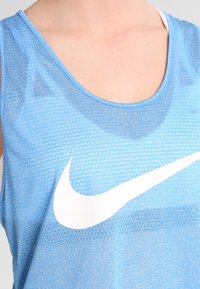 Jasnoniebieski sportowy top na ramiączkach z oddychającą siateczką, z dużym białym logo Nike w kształcie pioruna z przodu.