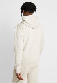Beige hoodie med dragsko i huvan, ribbade ärmar och nederkant. Mjuk textur, avslappnad passform och minimalistisk design. Inga synliga mönster eller detaljer.