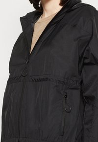 Svart lättviktsjacka med zip-up fram, elastisk midja och två sidofickor med zipperstängningar. Tillverkad av smidigt, vattentåligt material.