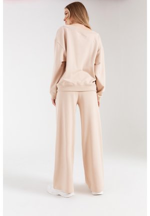 Beżowy zestaw odzieży do relaksu składający się z luznego swetra i szerokich spodni, wykonany z miękkiego materiału z prążkowanymi mankietami i paskiem w talii.