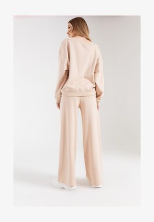 Beżowy zestaw odzieży do relaksu składający się z luznego swetra i szerokich spodni, wykonany z miękkiego materiału z prążkowanymi mankietami i paskiem w talii.