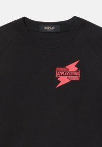 Čierna mikina s okrúhlym výstrihom a raglánovými rukávmi. Na prednej strane sa nachádza grafika červenej blesk s textom "REPLAY&SONS" v čiernych čiarach.