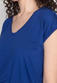 Blue v-neck top with short sleeves, made from a smooth, stretchy fabric. Features a relaxed fit and simple design without patterns or accents.