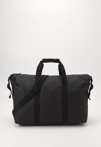 Sac de sport noir en matériau lisse et résistant à l'eau. Doté de poignées robustes, d'une bandoulière réglable et d'une fermeture zippée.
