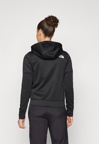 Black hooded sweatshirt made of smooth fabric. Features a fitted design, ribbed cuffs, and a white logo on the back.