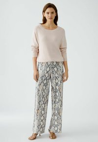 Lichtroze gebreide trui met een ruime halslijn, gecombineerd met losse slangenprint broeken in tinten wit, grijs en beige.