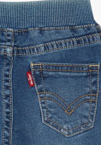 Blå denimjeansficka med orange sömmar och röd Levi's märkesetikett på det elastiska midjebandet.