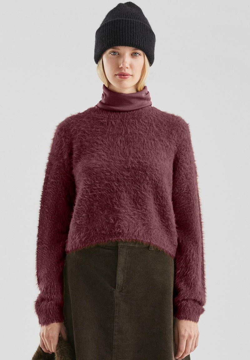 Bordeaux fuzzy trui met een hoge nek, gedragen over een donkere corduroy rok. Een zwarte gebreide beanie is ook zichtbaar. Zachte textuur opgemerkt.