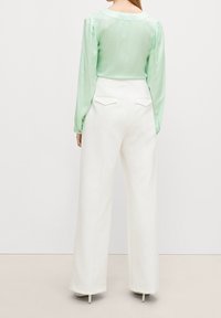Blusa a maniche lunghe verde menta con colletto arrotondato, abbinata a pantaloni bianchi a gamba larga con tasche posteriori e una texture liscia.