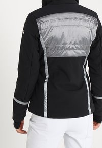 Schwarze Jacke mit einem silbernen, gepolsterten Rückenteil, körpernahem Schnitt und reflektierenden Akzenten entlang der Nähte und Bündchen. Glatte Textur.