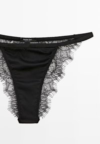 Perizoma nero con dettagli in pizzo intricati lungo i bordi. Tessuto morbido e liscio, con un'etichetta che riporta "Massimo Dutti."