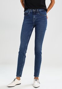 Jeans ajustados de mezclilla en azul con una cintura de altura media, que cuentan con bolsillos delanteros y traseros, combinados con zapatos oxford blancos.