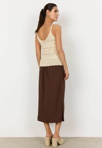 Canottiera in crochet beige con schiena alta, indossata con una gonna maxi marrone con spacchi laterali e sandali beige con tacco.