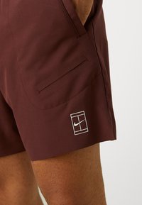 Bordeaux värvi Nike lühikesed püksid, mis on valmistatud siledast kangast, külgtasku ja valge logo ristküliku kujulisel taustal.