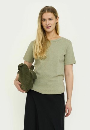 Olivgrünes Baumwoll-T-Shirt mit kurzen Ärmeln und rundem Ausschnitt, kombiniert mit einer grünen Wildledertasche mit einem Riemen und seitlichen Quasten.