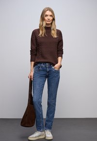 Suéter marrón de punto grueso, vaqueros azules de corte recto, zapatillas blancas y bolso de hombro de ante marrón. Diseño sencillo y texturizado.