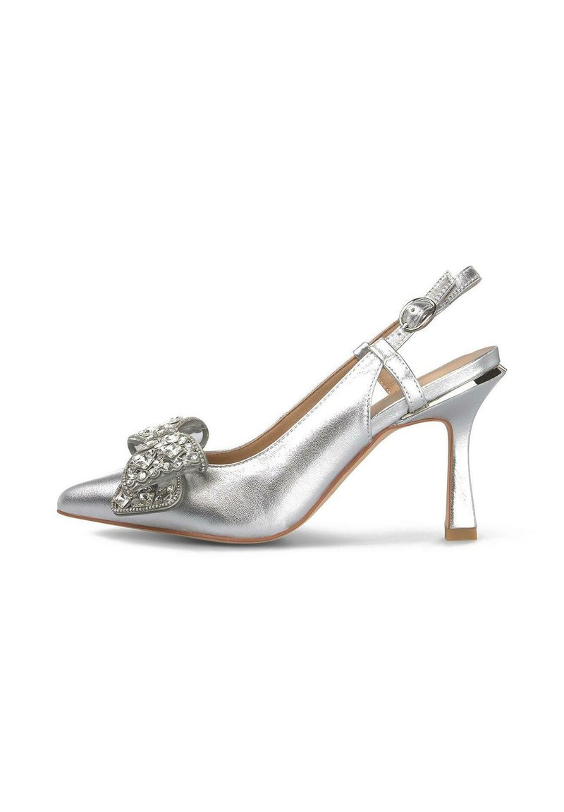 Zapatos de tacón con tiras al talón de color plata, con punta afilada, textura metálica, detalle de lazo decorativo y un tacón curvado y esbelto. Incluye un cierre con hebilla en la parte trasera.