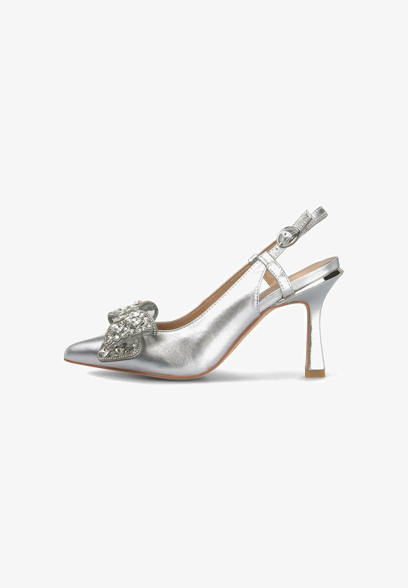 Zapatos de tacón con tiras al talón de color plata, con punta afilada, textura metálica, detalle de lazo decorativo y un tacón curvado y esbelto. Incluye un cierre con hebilla en la parte trasera.