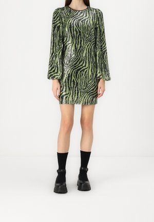 Robe à sequins verts et noirs avec un motif zèbre, manches bouffantes longues et encolure ronde. Portée avec des chaussettes montantes noires et des chaussures épaisses.