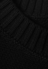 Gros plan sur un tissu noir tricoté montrant un col côtelé et un motif de maille texturé.