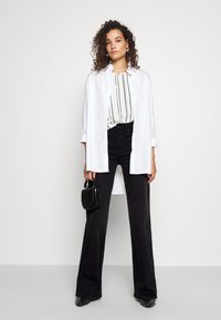 Valkoinen nappipaita kerrospukeutuneena mustavalkoraidallisen pystyraitaisen topin päälle; yhdistetty korkeavyötäröisiin mustiin liehuviin farkkuihin ja pieneen mustaan käsilaukkuun.