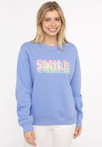 Hellblaues Sweatshirt mit gerippten Bündchen und Saum. Verziert mit dem Wort "SMILE" in bunten, fetten Lettern über die Brust. Weicher Stoff.