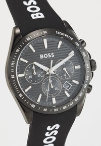 Black rubber strap watch featuring a textured gray dial, silver hour markers, three sub-dials, date display, and bold "BOSS" branding.