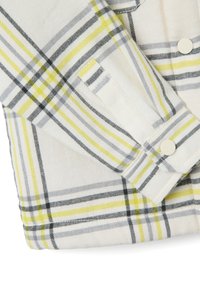 Camisa de cuadros blanca y amarilla con líneas grises y negras, con puños abotonados y una textura de tela suave.