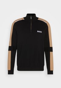 Pull noir zippé avec des rayures beiges sur les manches et le logo blanc "BOSS" sur la poitrine gauche, présenté sur un fond uni.