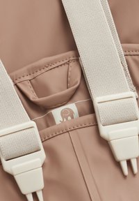 Lichtroze rugzak met een gestructureerde stof, crèmekleurige bandjes en een klein olifantenlogo op een label binnenin een zak. Inclusief verstelbare hardware.