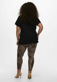 Crna oversized majica u kombinaciji s smešim tajicama sa leopard printom. Odjeća se ističe opuštenim krojem i dopunjena je bež visokim potpeticama.