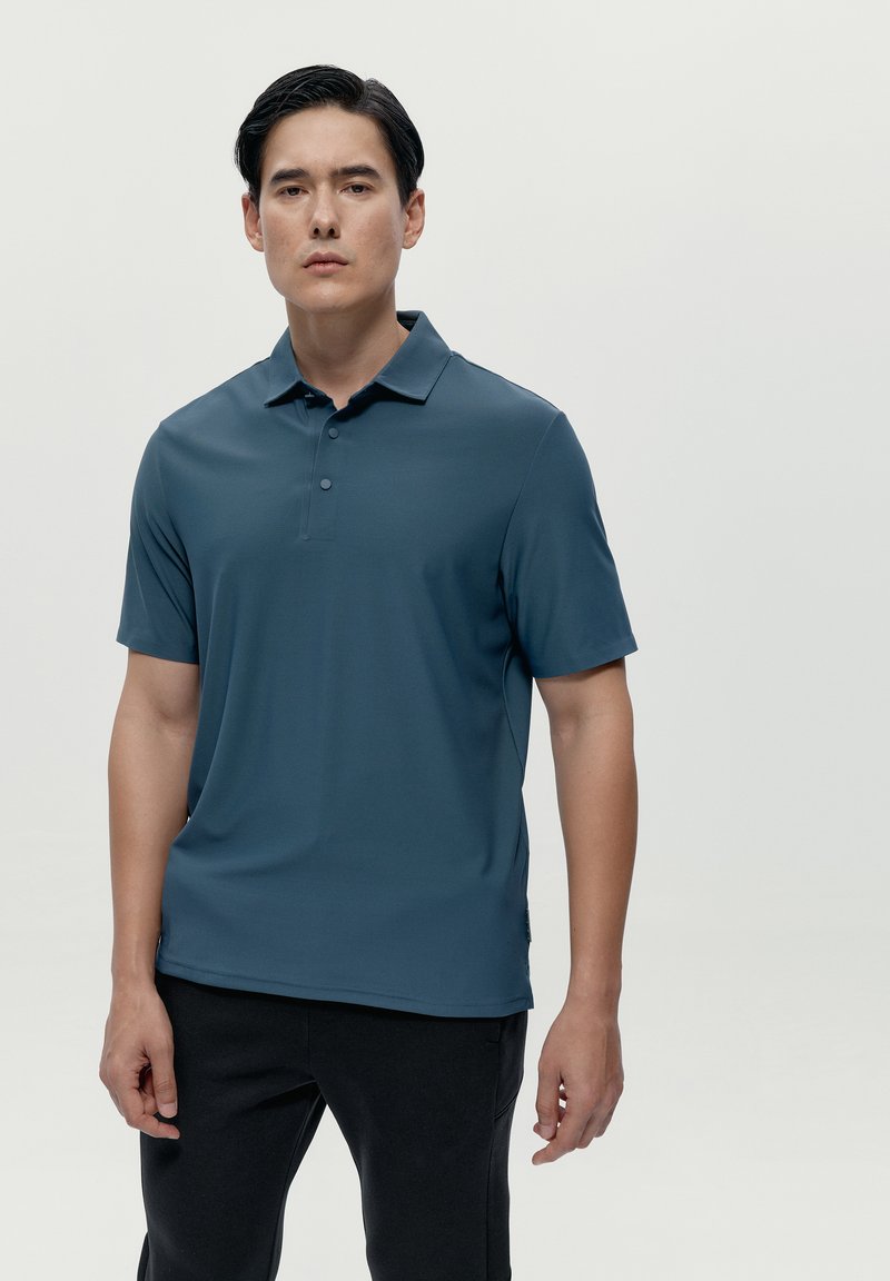 Polo a maniche corte da uomo in verde scuro, realizzato in tessuto morbido e traspirante. Presenta un colletto classico e una chiusura con tre bottoni.