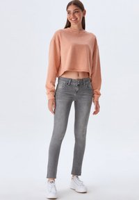 Un sweat-shirt court rose pâle, un jean slim gris et des baskets blanches. La tenue comprend des manches longues, une coupe décontractée et une texture lisse.