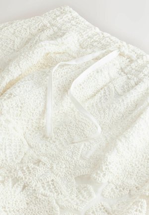 White crochet fabric featuring textured patterns and a drawstring closure. Soft, lightweight material with intricate detailing.