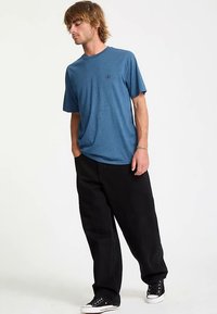 T-shirt blu a maniche corte con scollo rotondo e piccolo logo, abbinata a pantaloni neri larghi e sneakers nere.