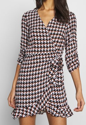 Vestido cruzado de pata de gallo en blanco y negro con detalles en naranja, mangas tres cuartos y volante en el dobladillo y la cintura. Textura de tela suave.