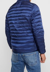 Donkerblauw doorgestikt jack met een hoge kraag, een gladde textuur en zichtbare stikdetails, gecombineerd met spijkerbroeken.