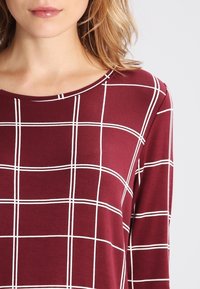 Burgunderfarbenes Langarmshirt mit einem weißen Gittermuster, Rundhalsausschnitt und weicher, glatter Textur. Hat Details für einen lässigen, entspannten Schnitt.