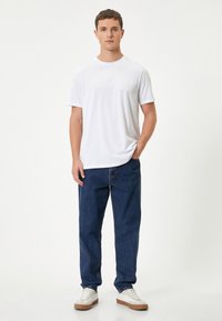 Hvid t-shirt med rund hals, parret med løstsiddende mørke denimjeans og hvide sneakers med lysebrune accenter. Glat stof, afslappet stil.