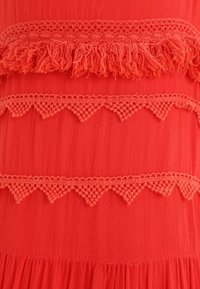 Rode stof met textuurlaagjes, voorzien van franjes en gehaakte accenten in een zigzagpatroon, wat een gelaagd ontwerp effect creëert.