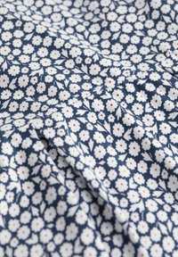 Námořnická látka s hustým bílým květinovým vzorem a malými červenými tečkami. Textura se zdá být hladká a lehká.