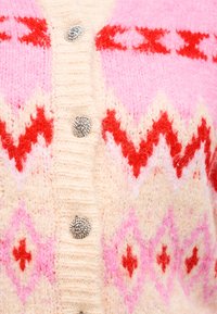 Μαλακό πλεκτό ζακέτα με ζιγκ-ζαγκ και διαμαντένια σχέδια σε κόκκινο, ροζ και εκρού, με υφασμένα ασημένια στρογγυλά κουμπιά κατά μήκος του κέντρου.