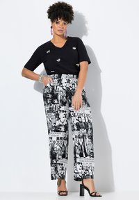 Zwarte v-hals t-shirt met decoratieve accenten, gecombineerd met opvallende, brede broek in zwart en wit met grafische prints en tekst.