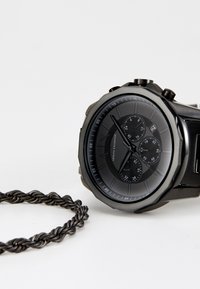 Orologio analogico nero con più sottodial, cassa ottagonale, dettagli argentati e bracciale intrecciato nero texturizzato.