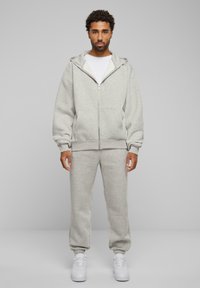 Grå fleece zip-up hoodie med stor hætte og forlommer, parret med matchende tapered sweatpants og hvide sneakers.